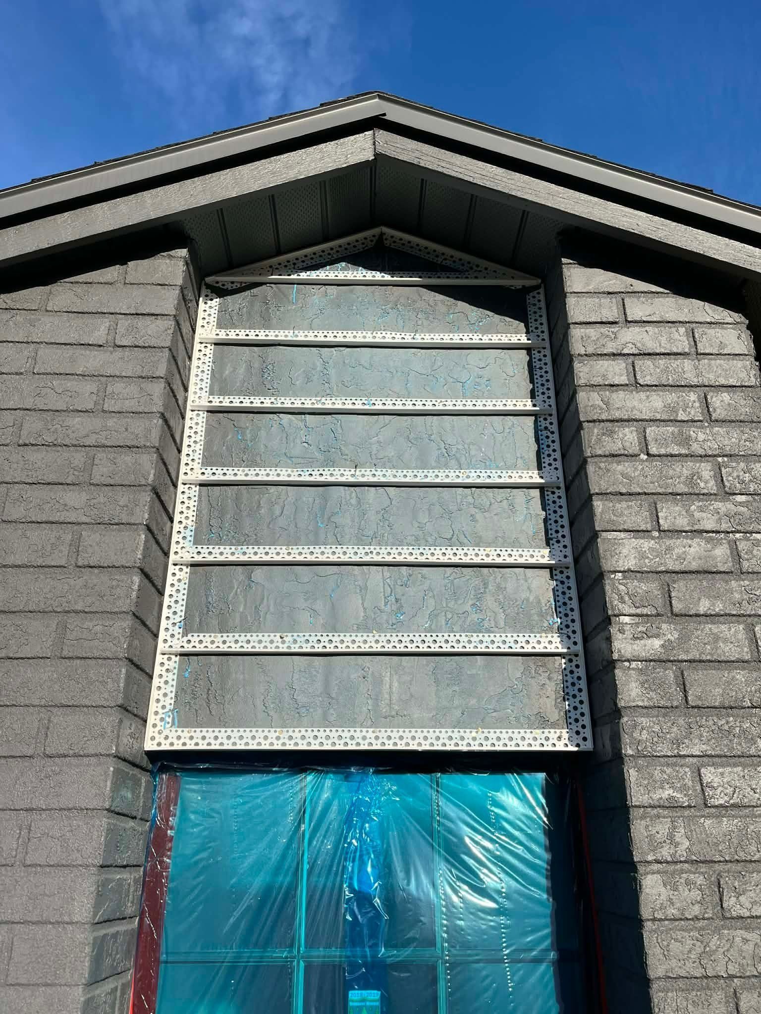 Small house gable with white louvered vent and blue plastic-covered opening beneath it