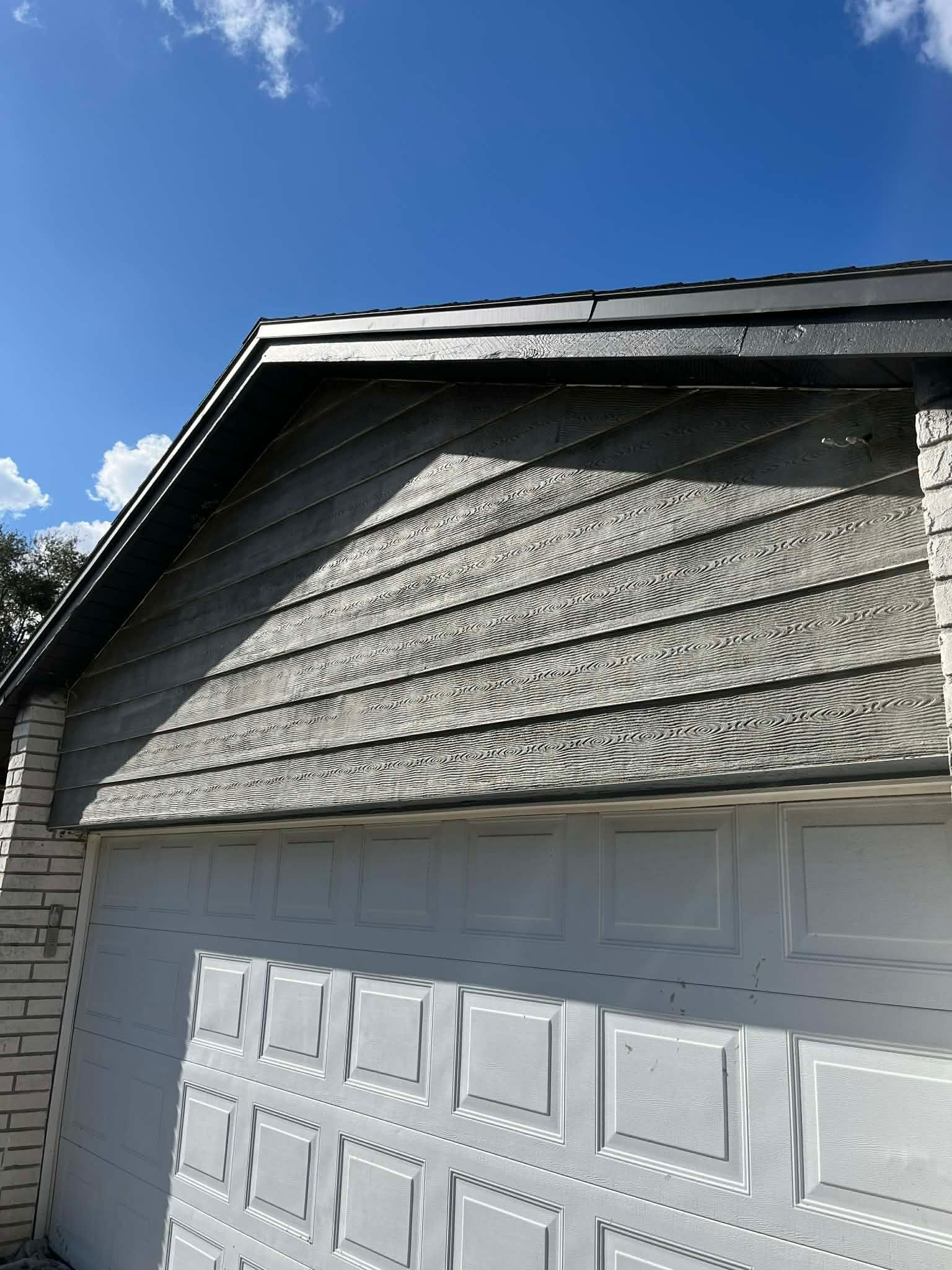 Close-up of a house gable with gray shingle siding above a white garage door under a blue sky