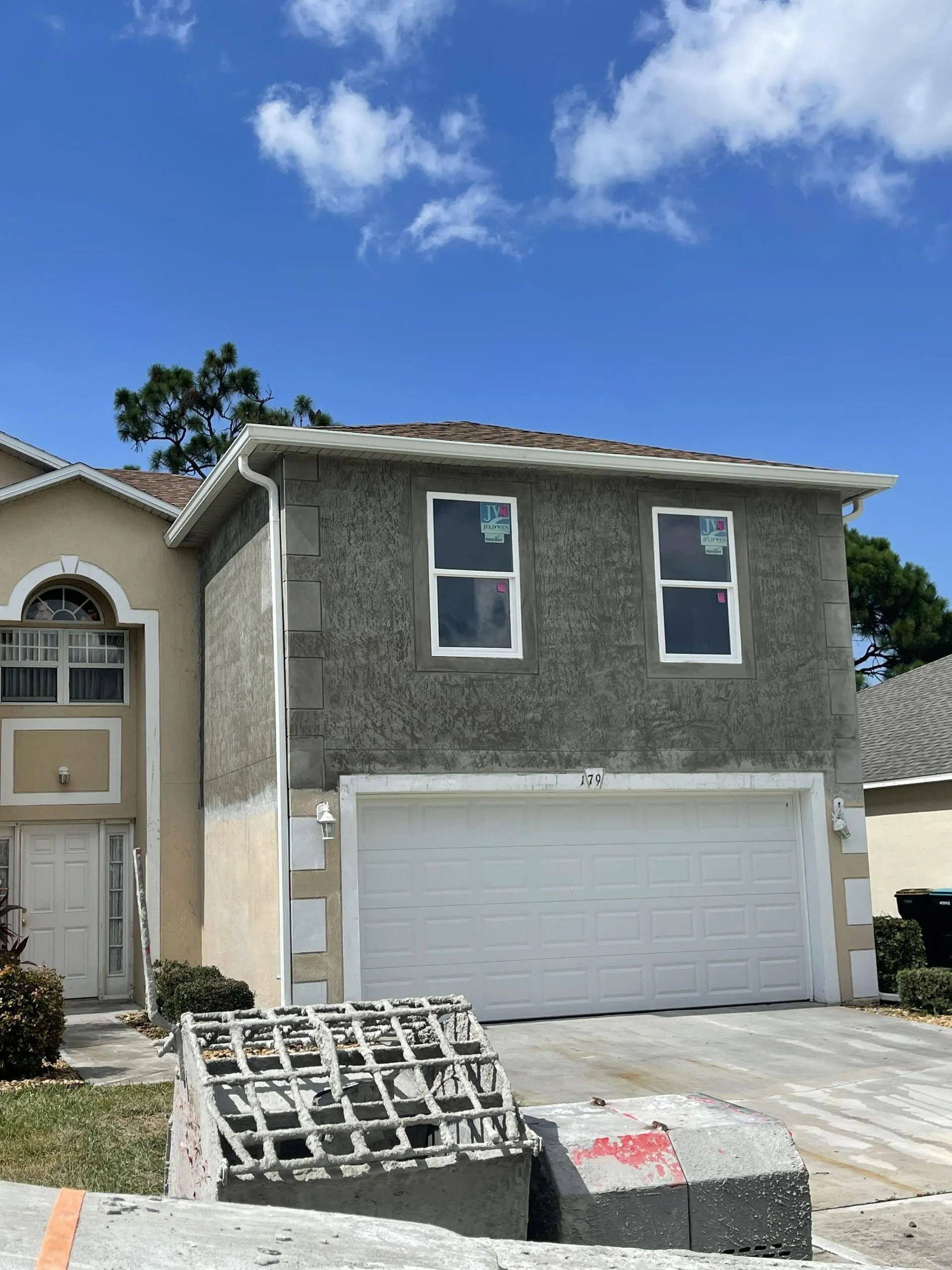 Two-story house with a white garage and a small construction dumpster in front under a blue sky