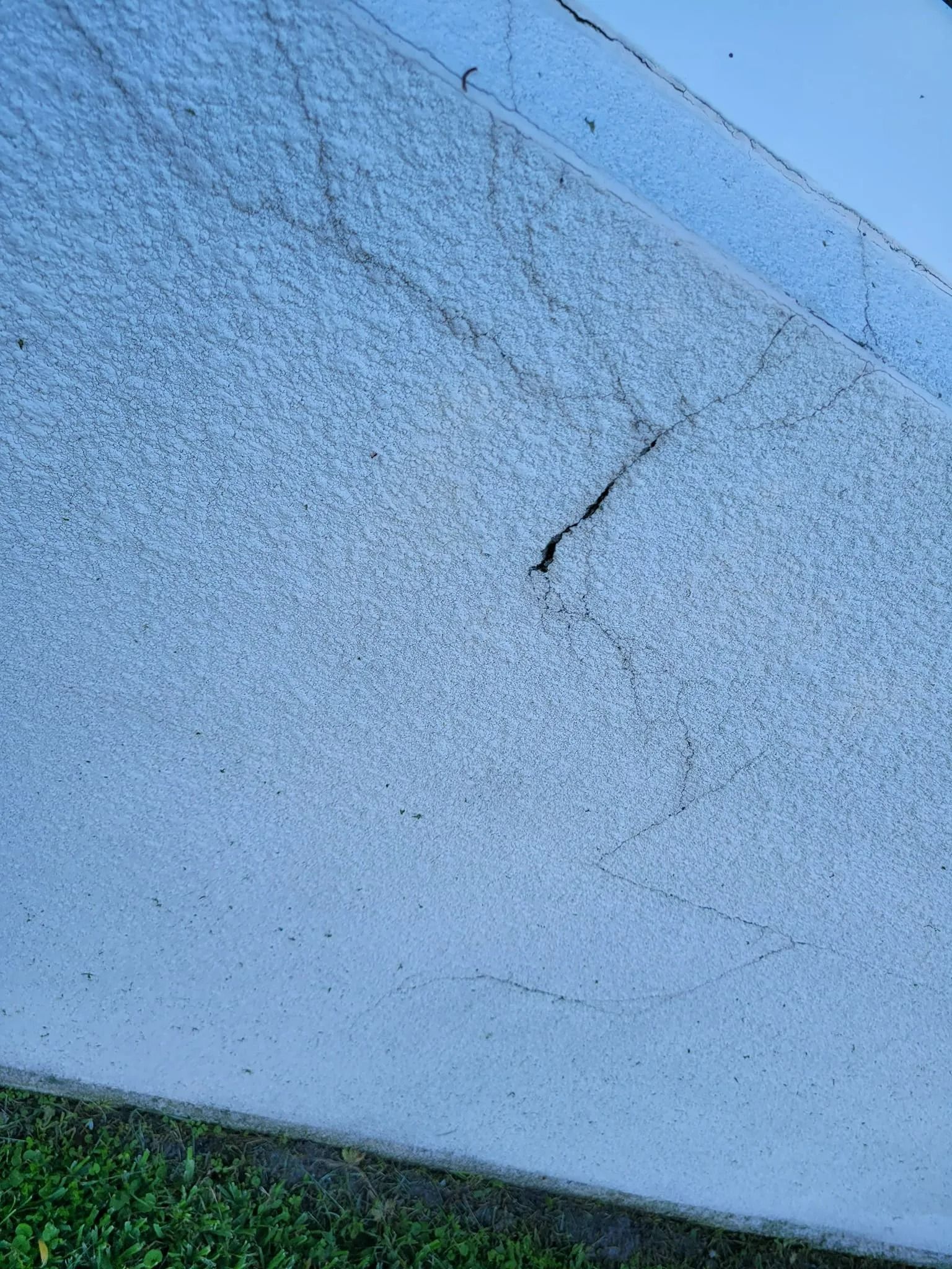 Close-up of a blue concrete wall with a visible crack and green grass at the bottom edge