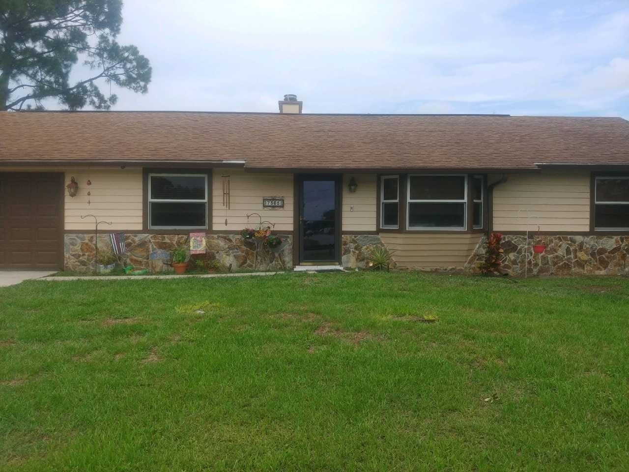Single-story house with tan siding, blue front door, stone base, and a large green lawn.