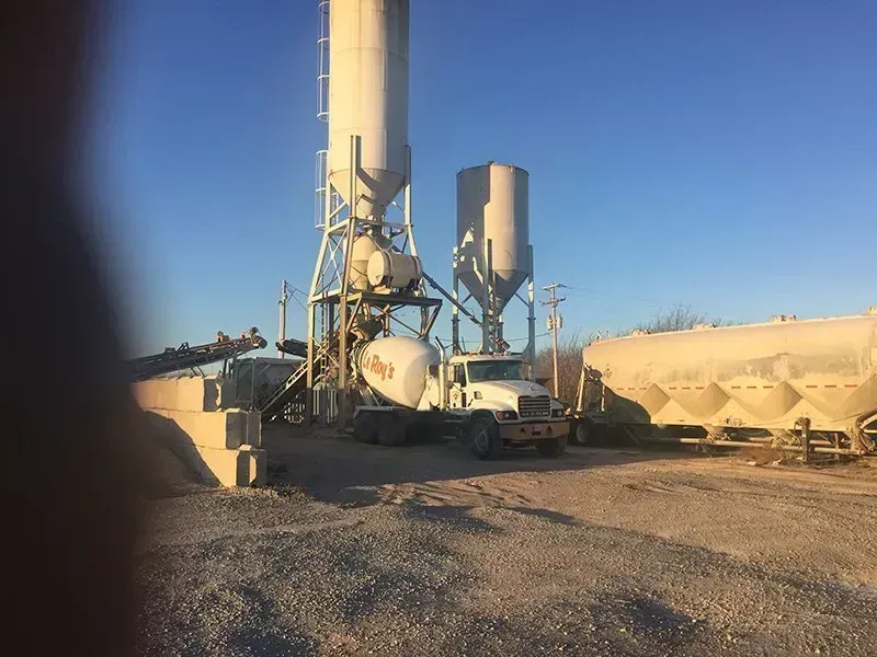 Industrial site with tall metal silos, pipes, and tanks under a clear blue sky