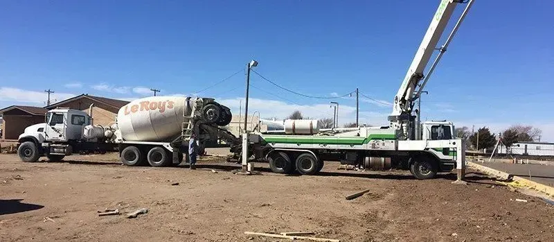Concrete mixer trucks and a crane in a dusty construction yard under a clear blue sky