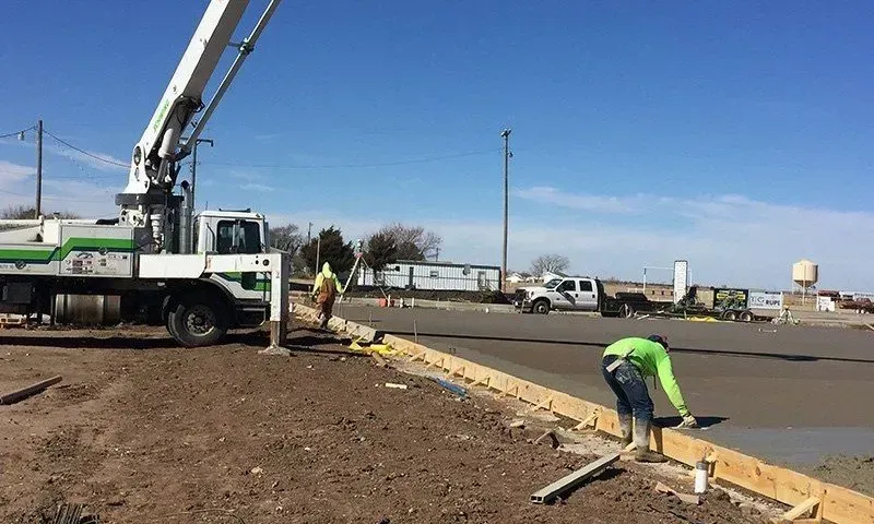 Road workers laying concrete curb beside a crane truck at a roadside construction site.