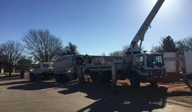 Utility trucks and a crane parked roadside in bright sunlight, with one worker in a truck cab.