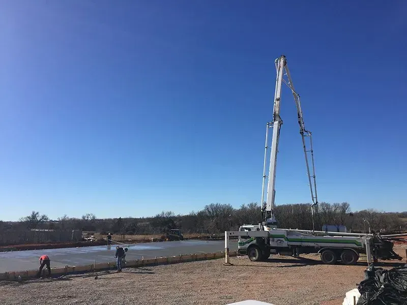 Concrete pump truck pouring at a roadside construction site under a clear blue sky