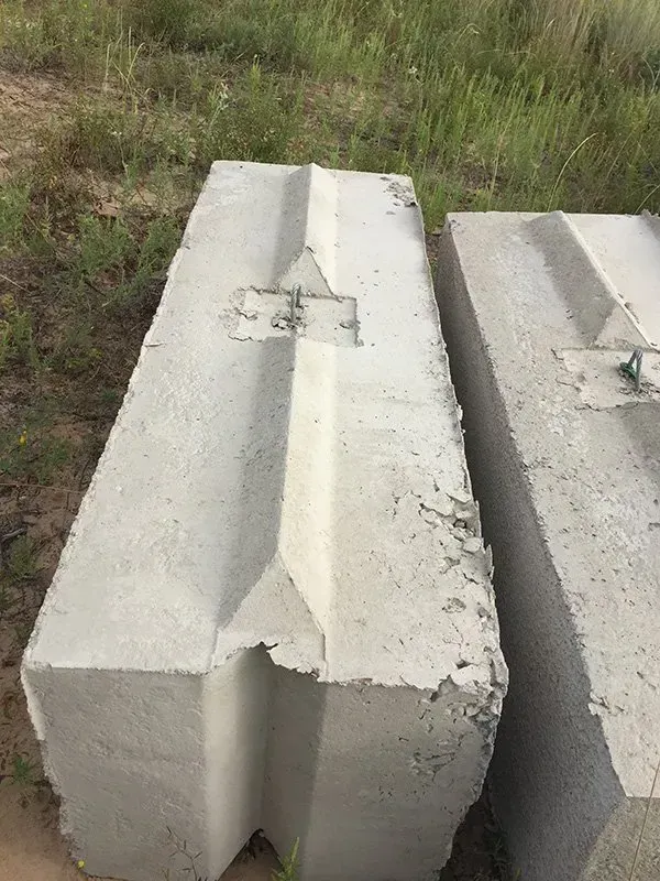Two cracked gray concrete barriers on grass, one with a broken corner and center patch.