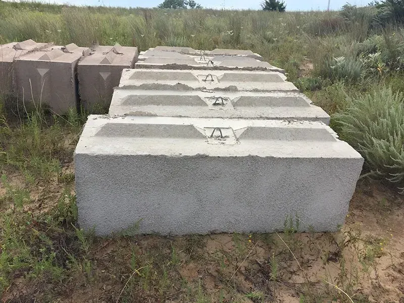 Rows of concrete blocks stacked outdoors in a grassy field under cloudy light