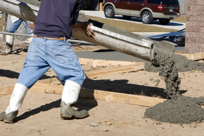 Worker pouring wet concrete from a mixer truck onto a construction site.