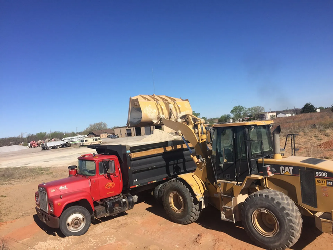 Yellow loader dumping dirt into red dump truck at a construction site under a clear blue sky