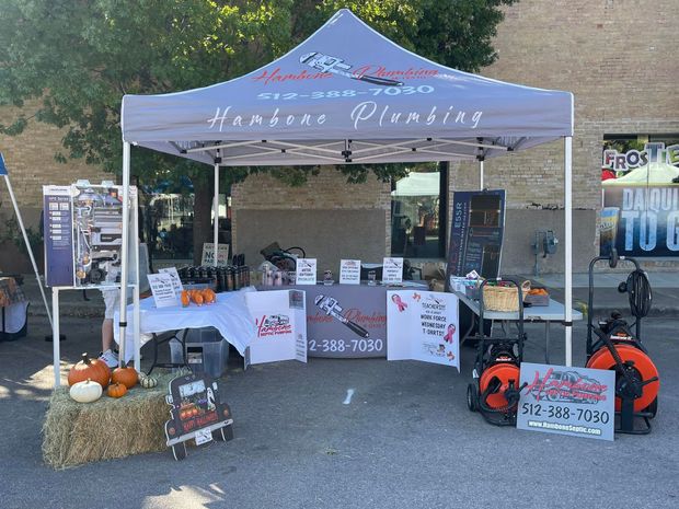 Outdoor market booth with blue canopy, table displays, pumpkins, and fall decor for Hanson Plumbing.