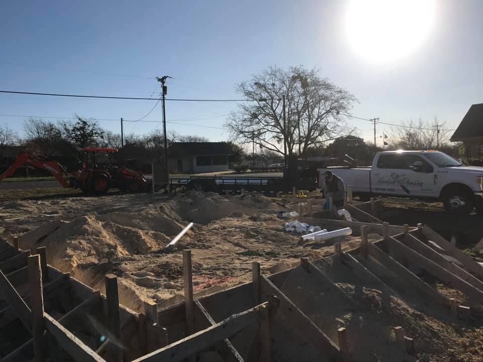Construction site with a dug-out foundation, wooden forms, pickup truck, and bright sun in the background