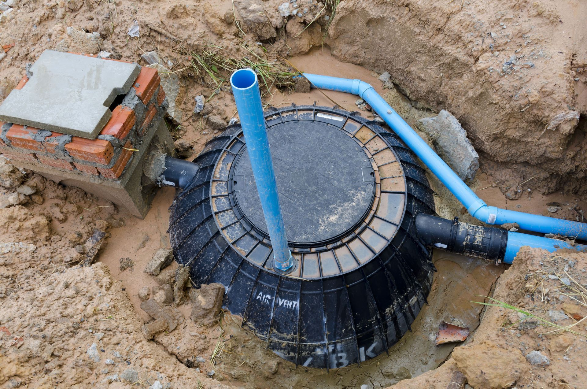 Underground septic tank installation with blue PVC pipes and a brick inspection chamber.