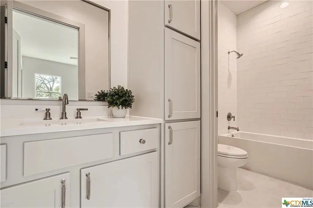 Bright white bathroom with double vanity, large mirror, storage cabinet, and tub-shower combo