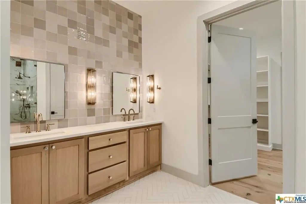 Modern bathroom vanity with double sinks, wood cabinets, mirrors, and an open door to a tiled shower room