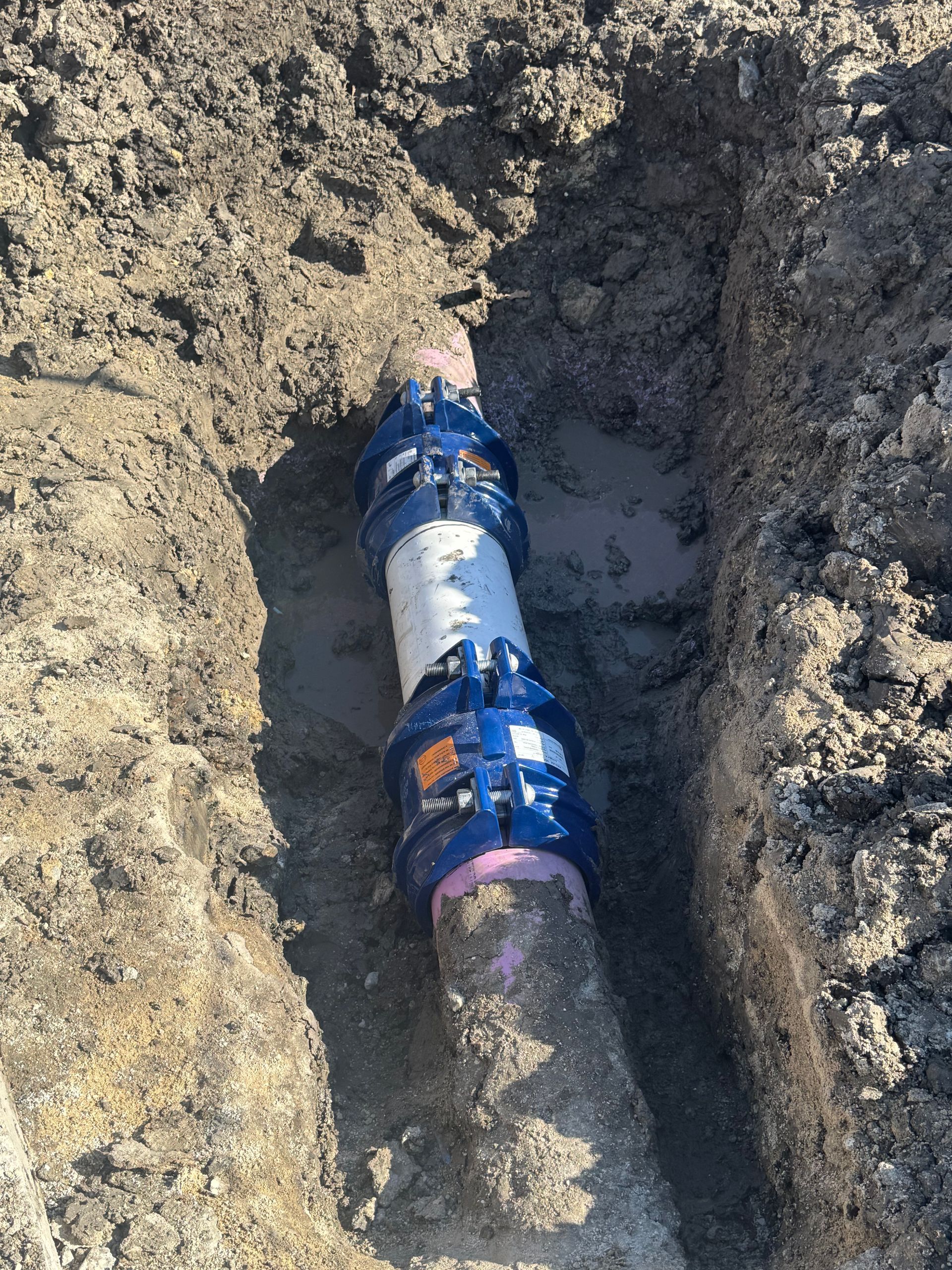 Broken blue water pipe in a dirt trench leaking water at a construction site