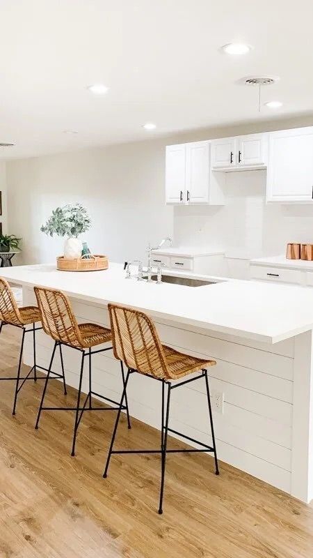 Bright modern kitchen with white island, wicker bar stools, wood floors, and built-in cabinetry