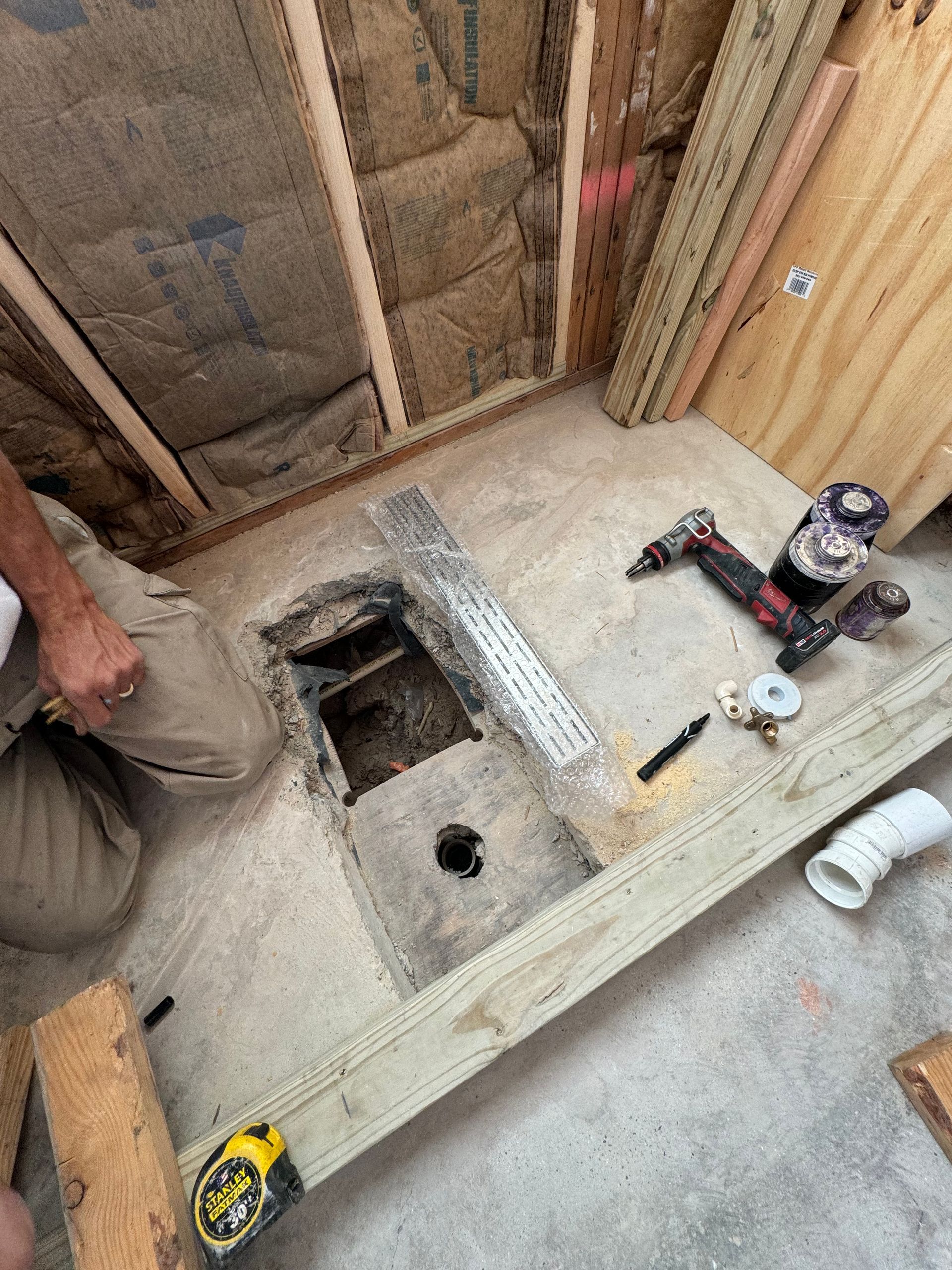 Construction area with exposed floor joists, tools, and a person kneeling beside a floor opening.