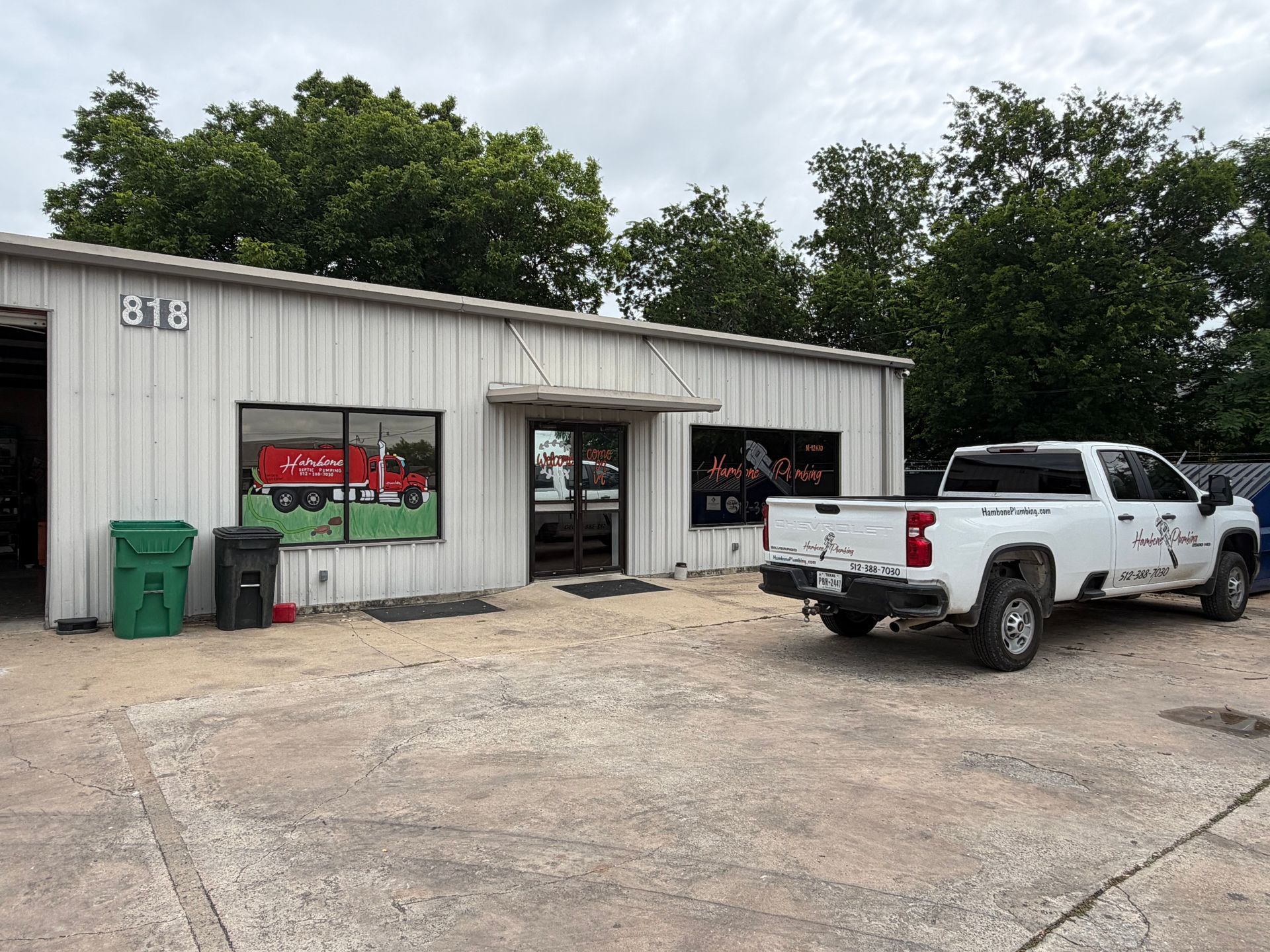 White pickup parked outside a small auto shop with open garage bays and green trash bins