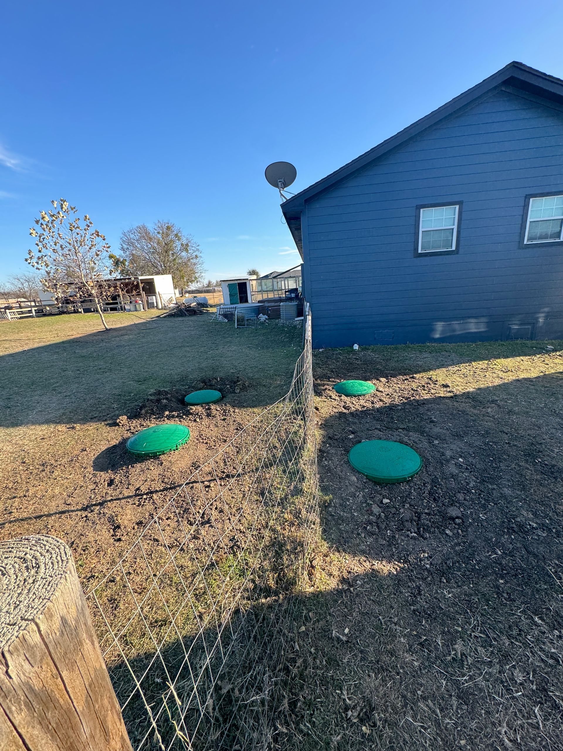 Blue house with gravel yard, green covers, and a chain-link fence under a clear sky.