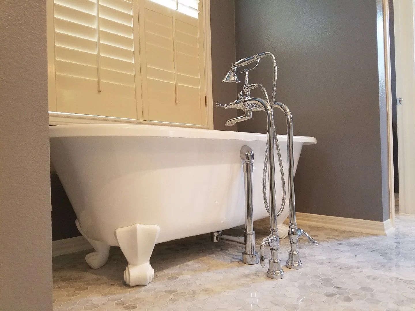 White clawfoot bathtub with chrome faucet in a bathroom near a window with blinds.