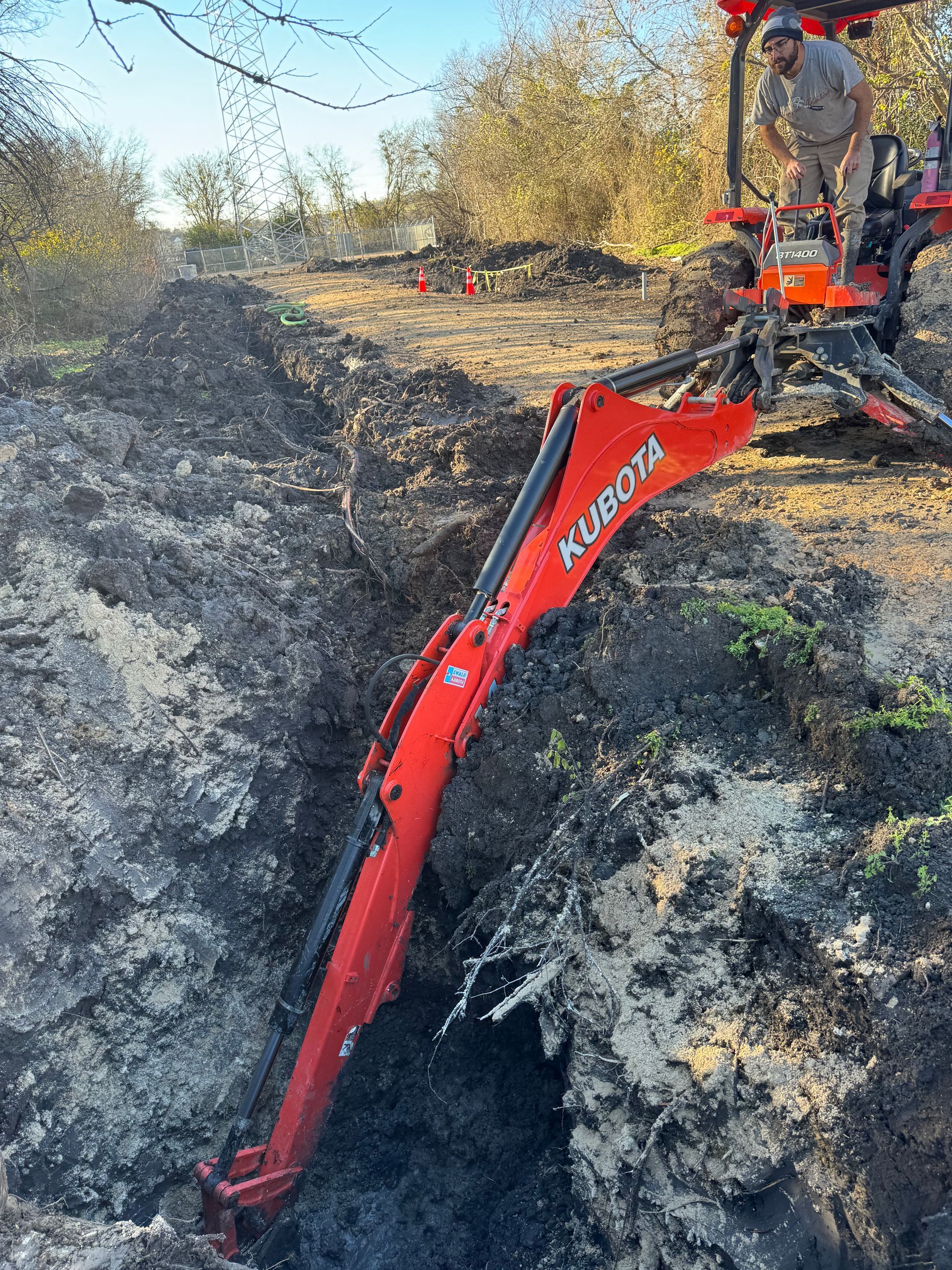 Red excavator arm digging into a deep trench in rocky ground outdoors
