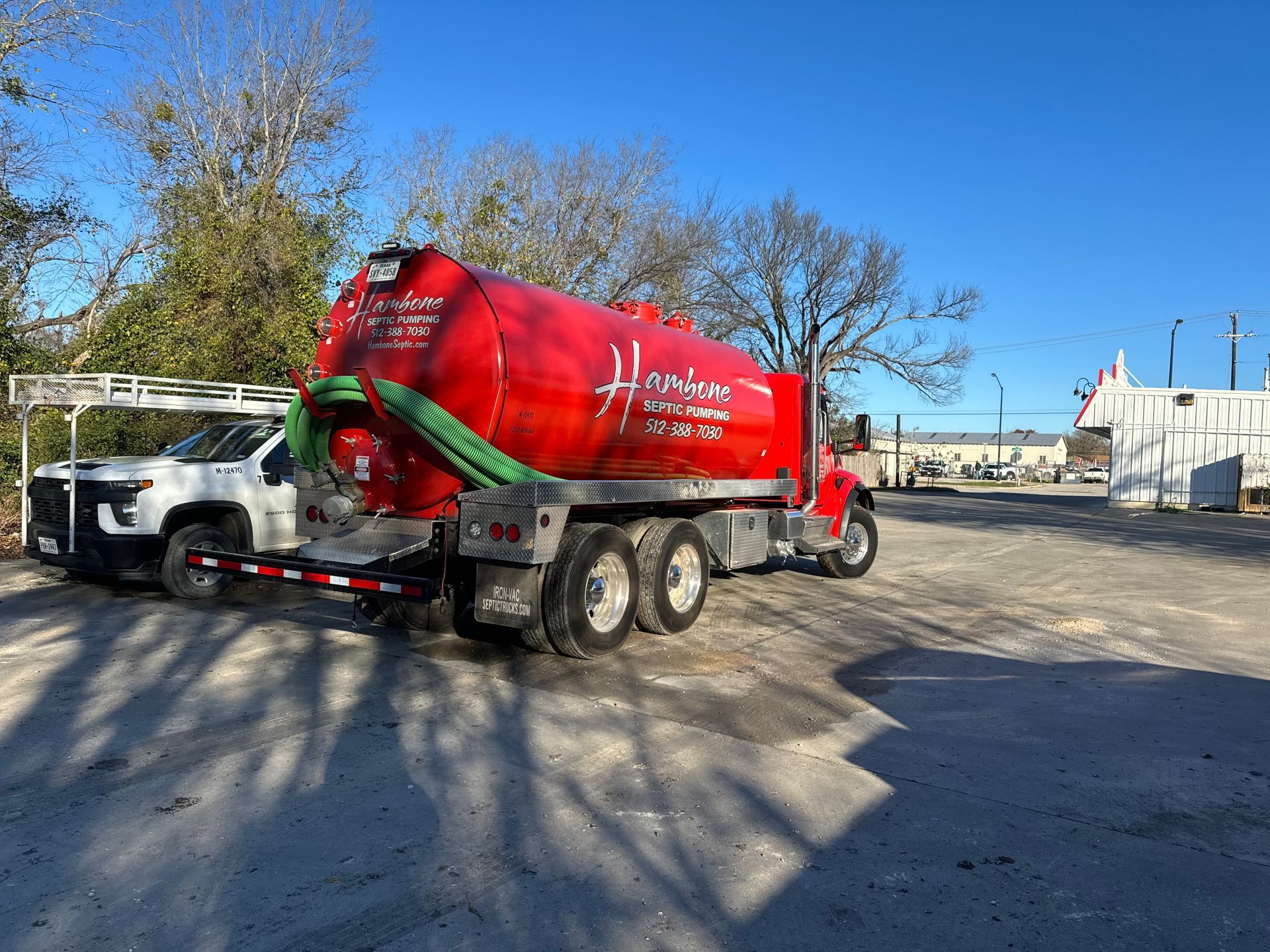 Red cement mixer truck parked in a gravel lot under a clear blue sky