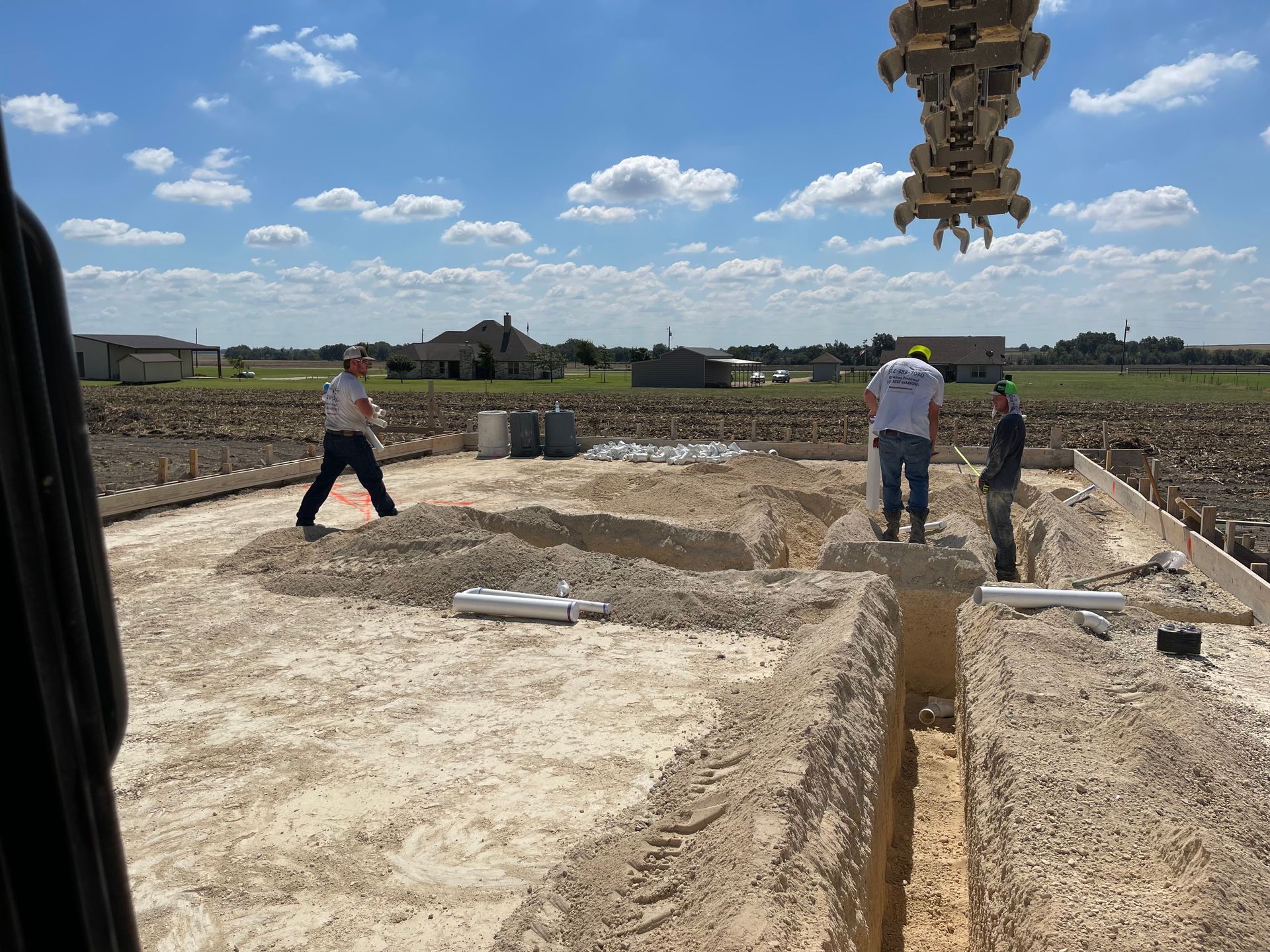 Workers inspect concrete foundation trenches at a construction site under a blue sky.