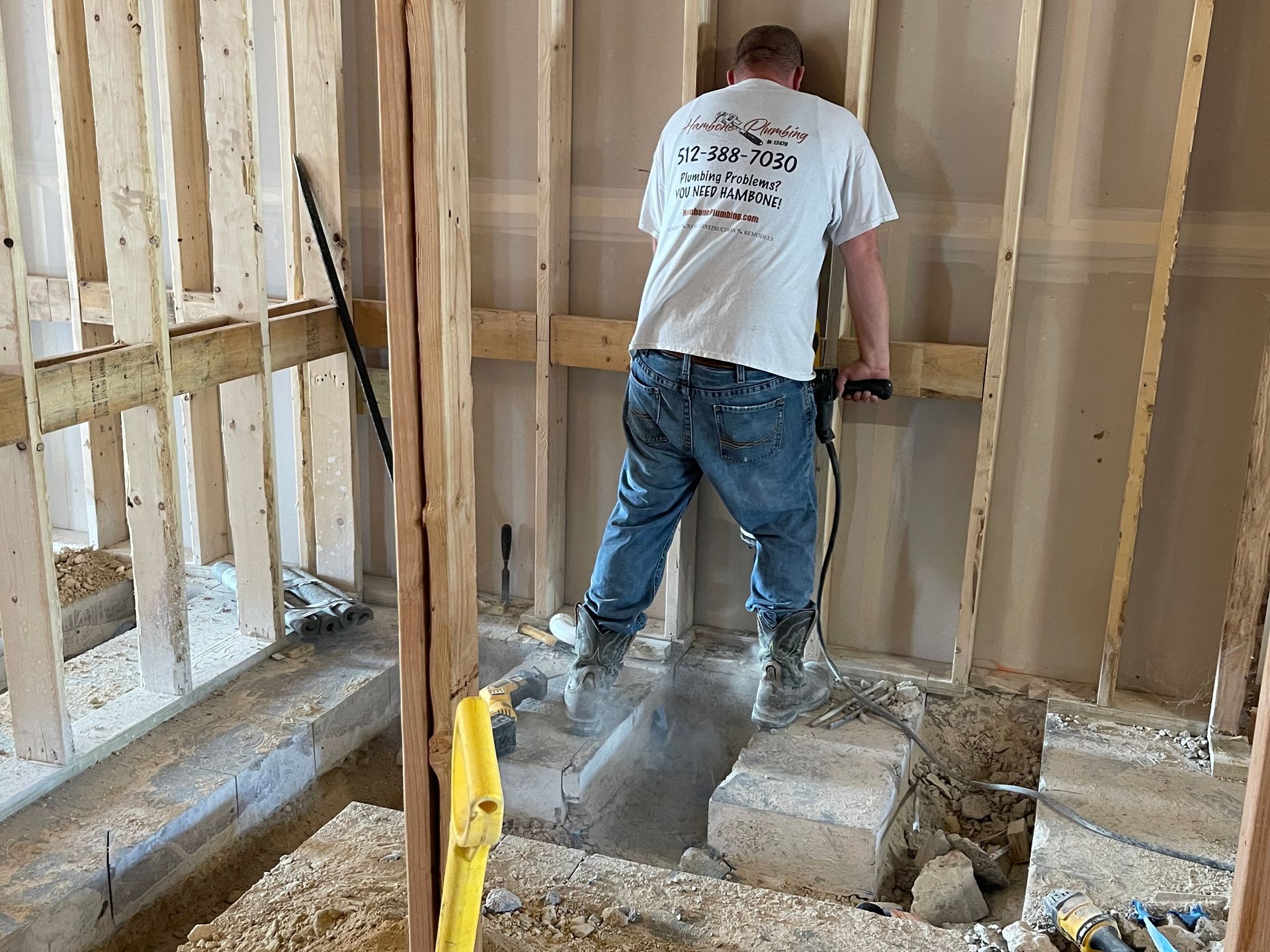 Worker in a partially framed room using a power tool amid dust and debris