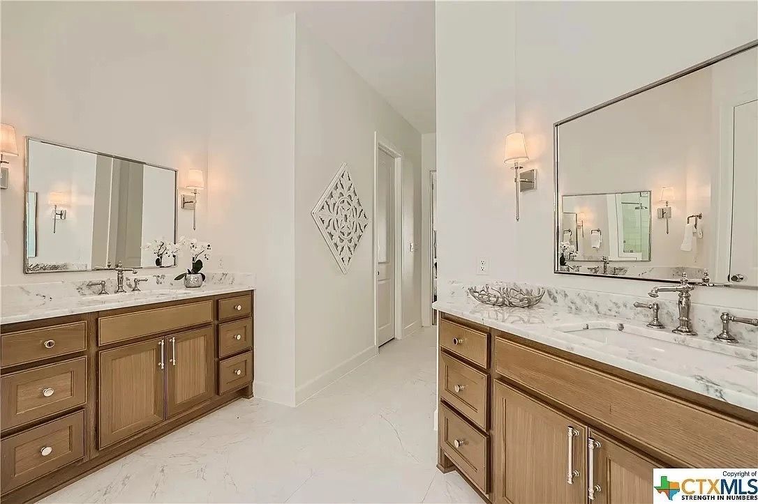 Bright bathroom with double wood vanities, marble countertops, mirrors, and wall sconces