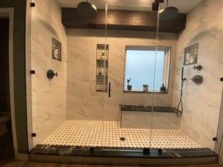 Modern walk-in shower with beige tiled walls, black fixtures, and a small window shelf.