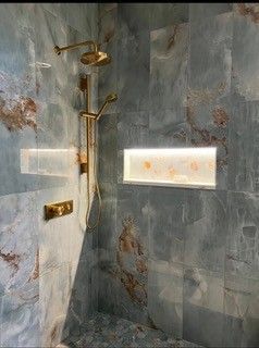 Modern bathroom shower with gray marble tiles, gold fixtures, and a small frosted window.