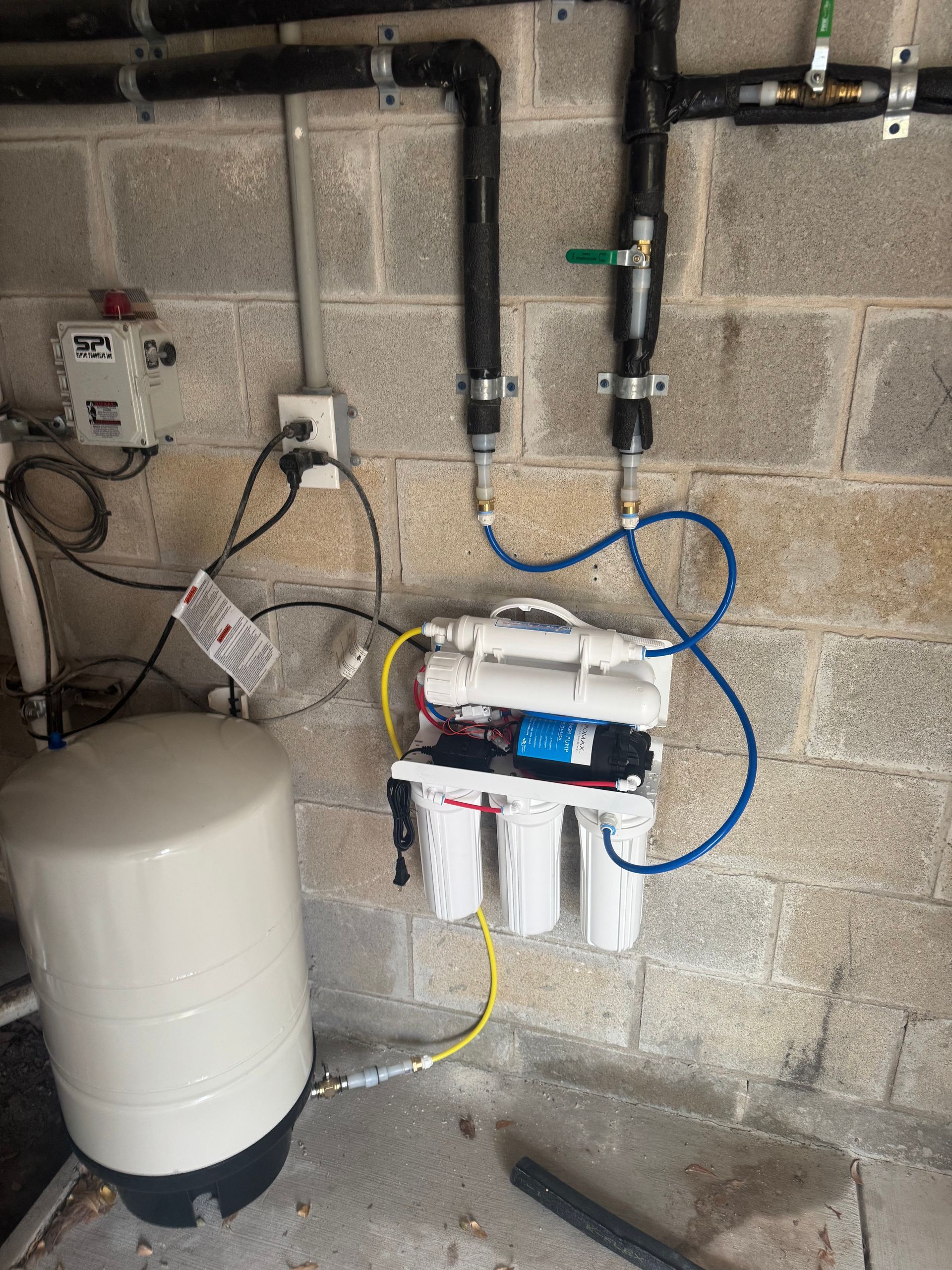 Water treatment/filtration system with pipes, pressure tank, and filter canisters against a cinderblock wall.