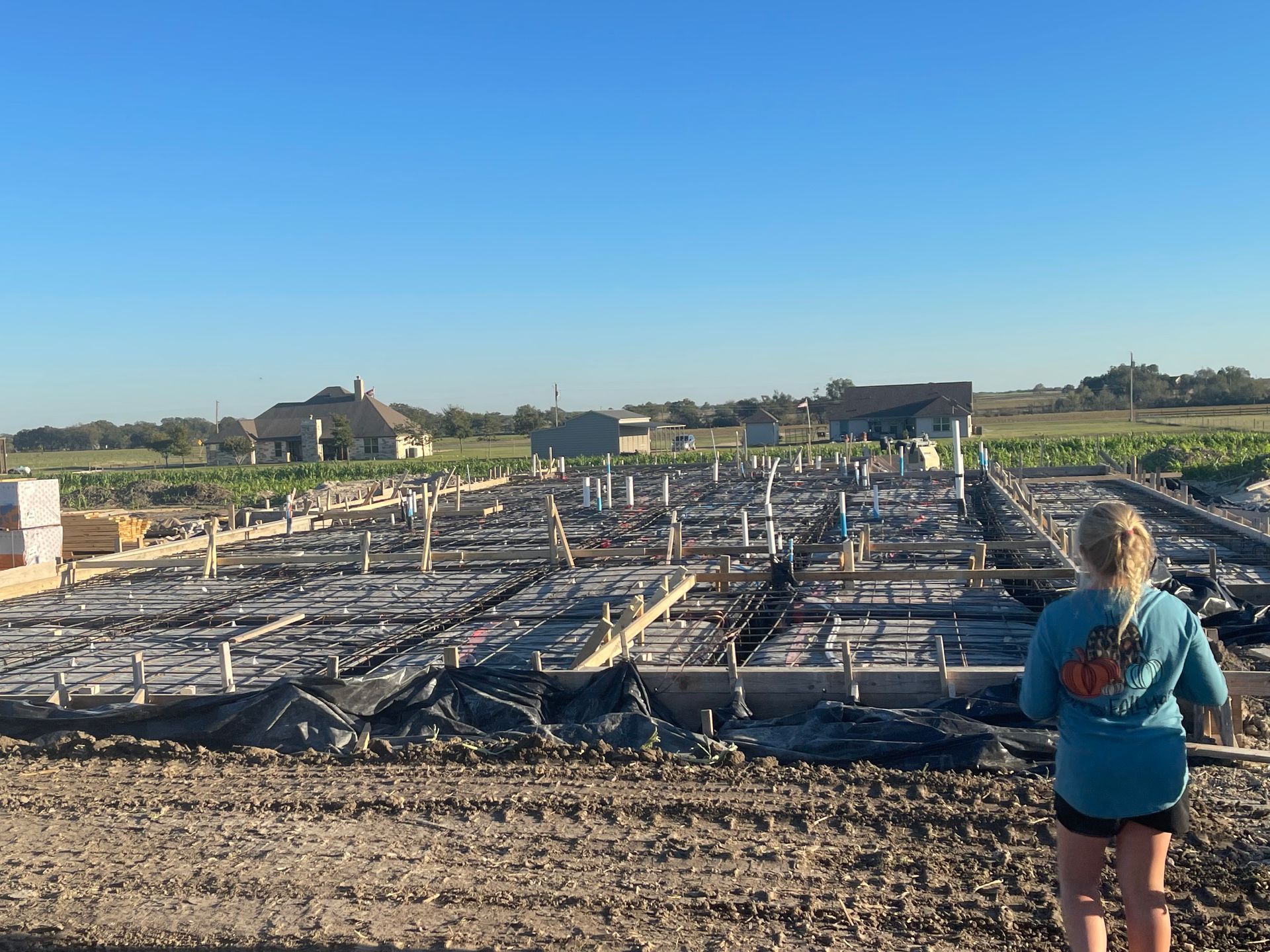 Person overlooking a flooded construction site with rebar and wooden forms under a clear blue sky