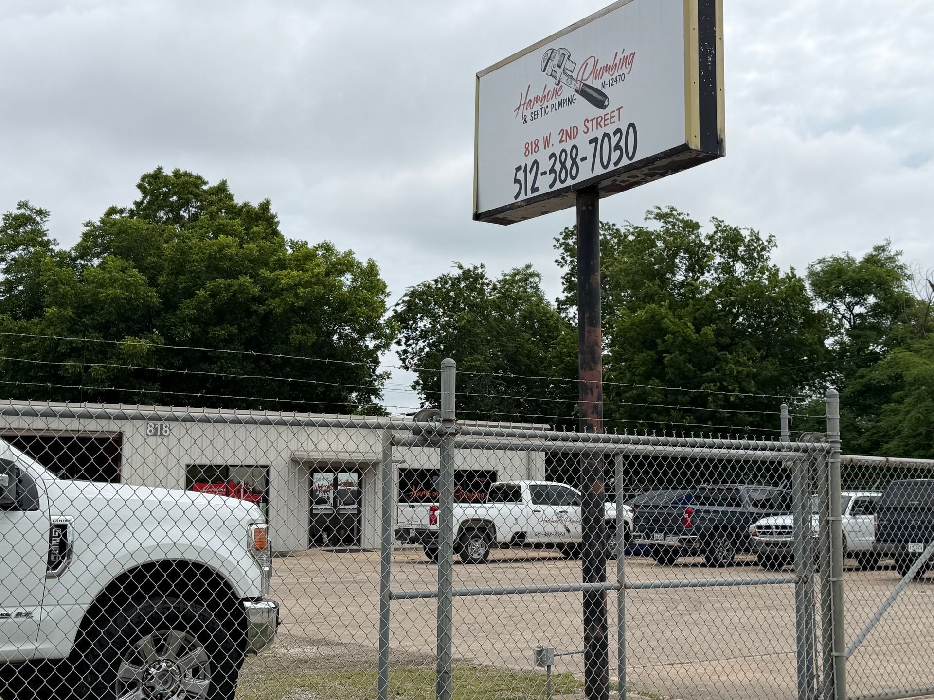 Chain-link fence in front of a car lot with parked vehicles and a large roadside sign.