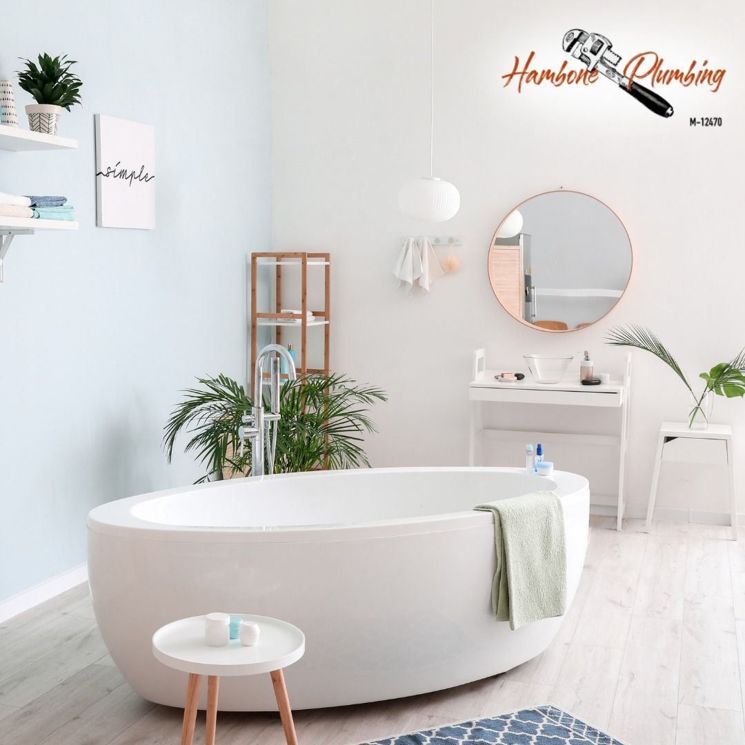 Bright minimalist bathroom with a white oval tub, vanity, round mirror, and plants on pale wood floors