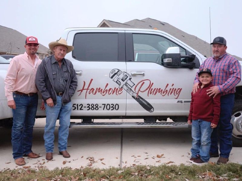 Three people beside a white plumbing service van with a child in front, outside a house