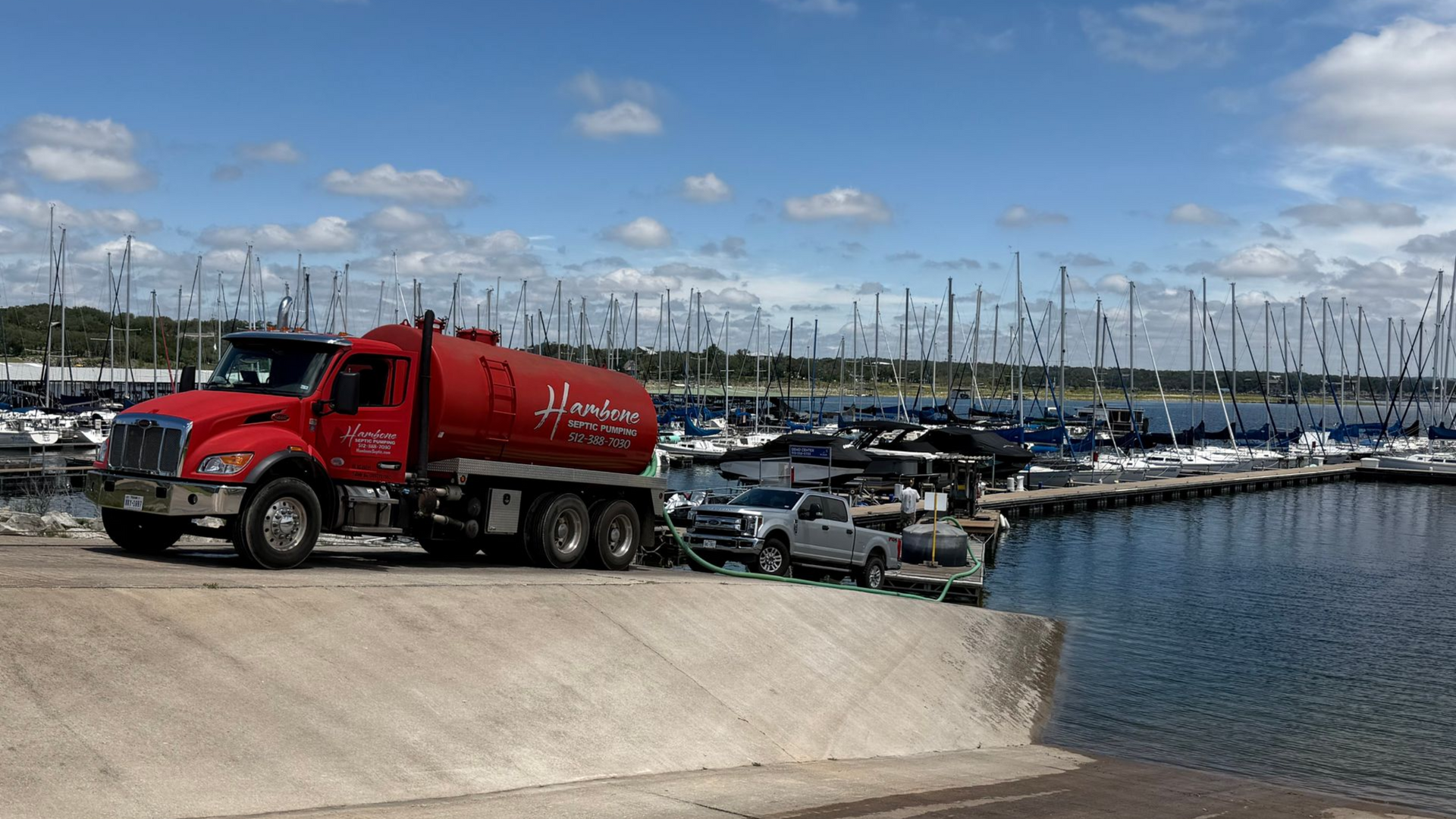 Red fuel truck parked beside a marina full of boats under a cloudy sky