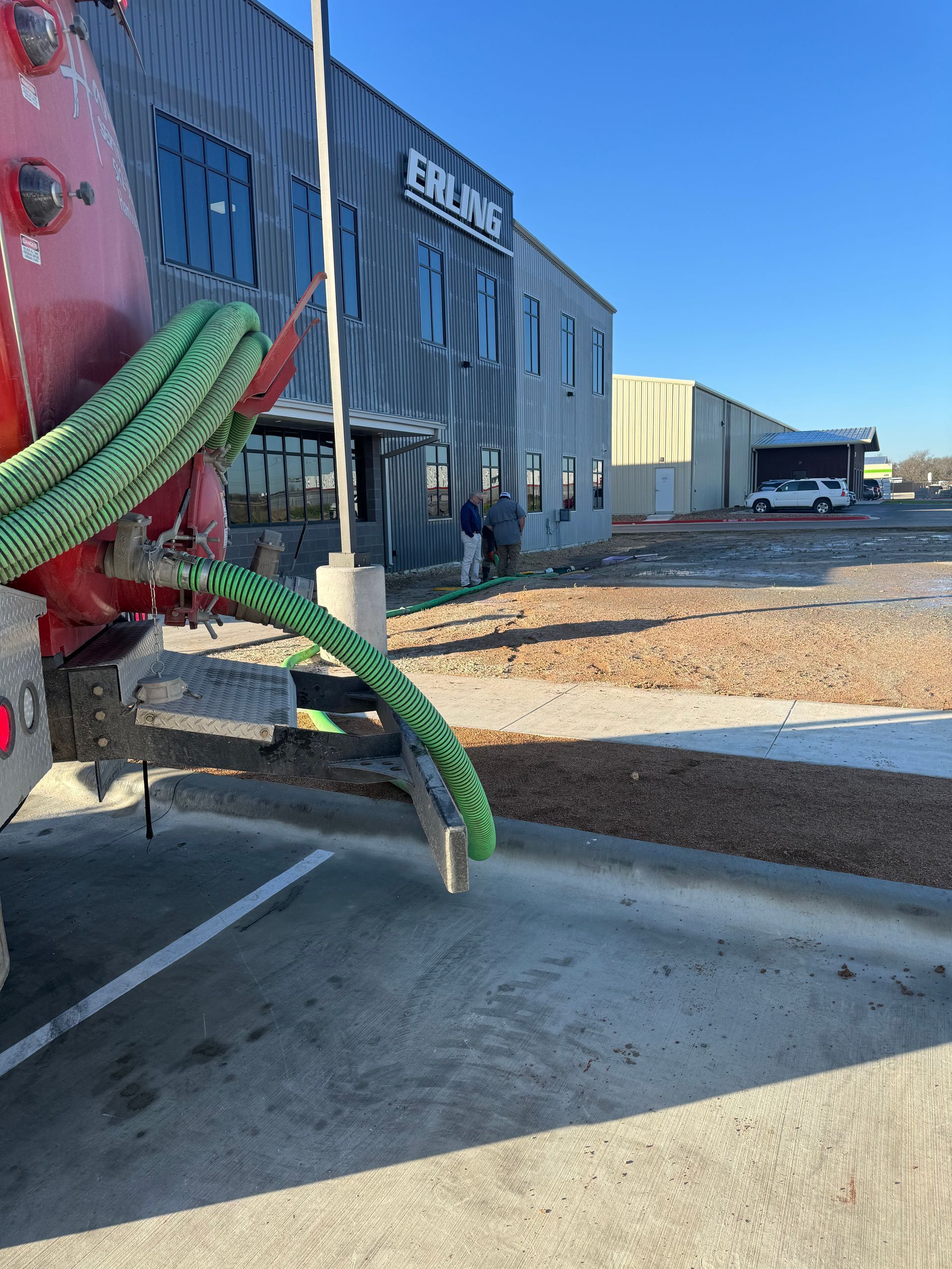 Industrial yard with a red truck, green hoses, and blue warehouse buildings under clear skies