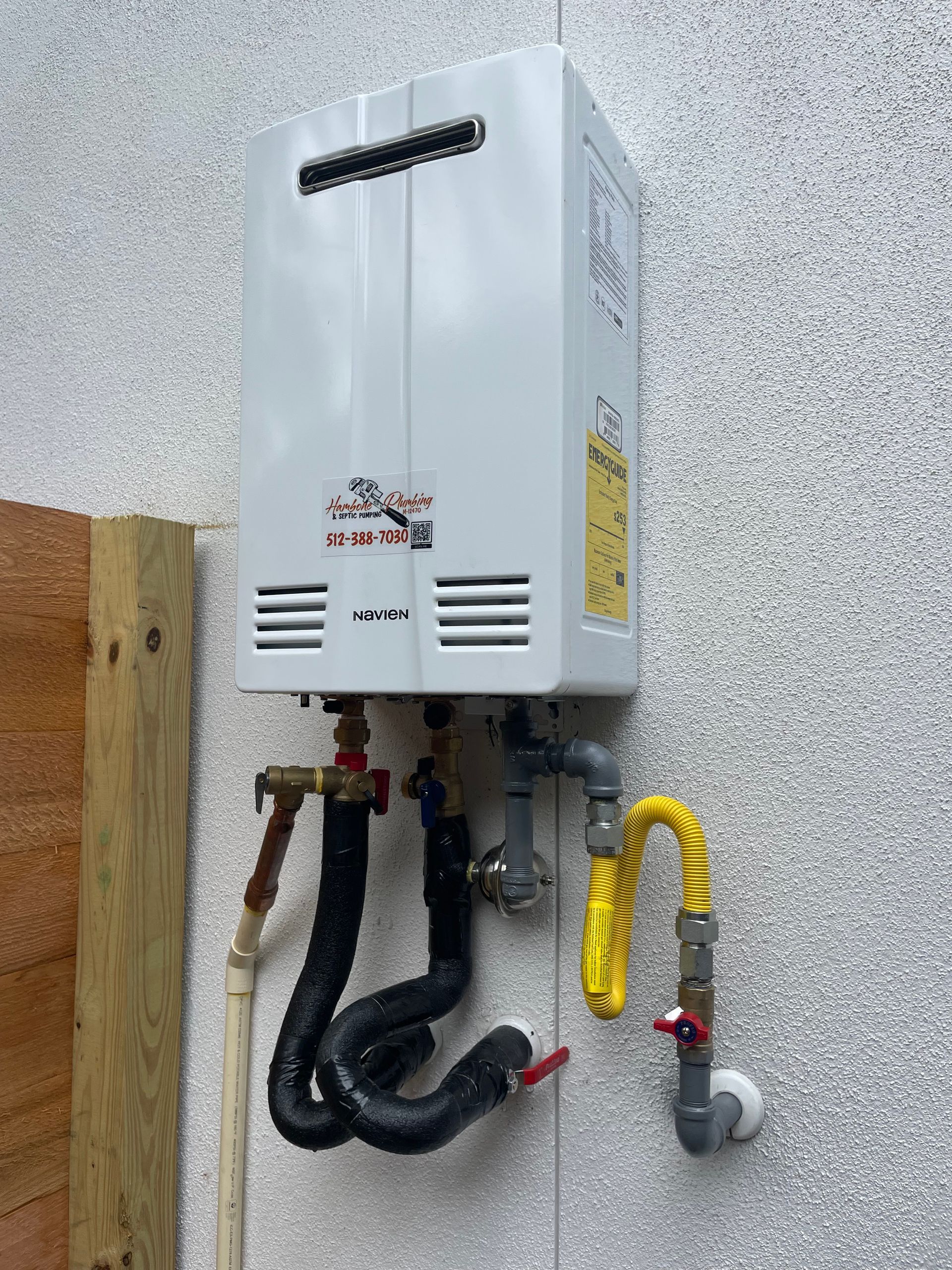 Wall-mounted gas water heater with pipes and valves against a textured exterior wall.