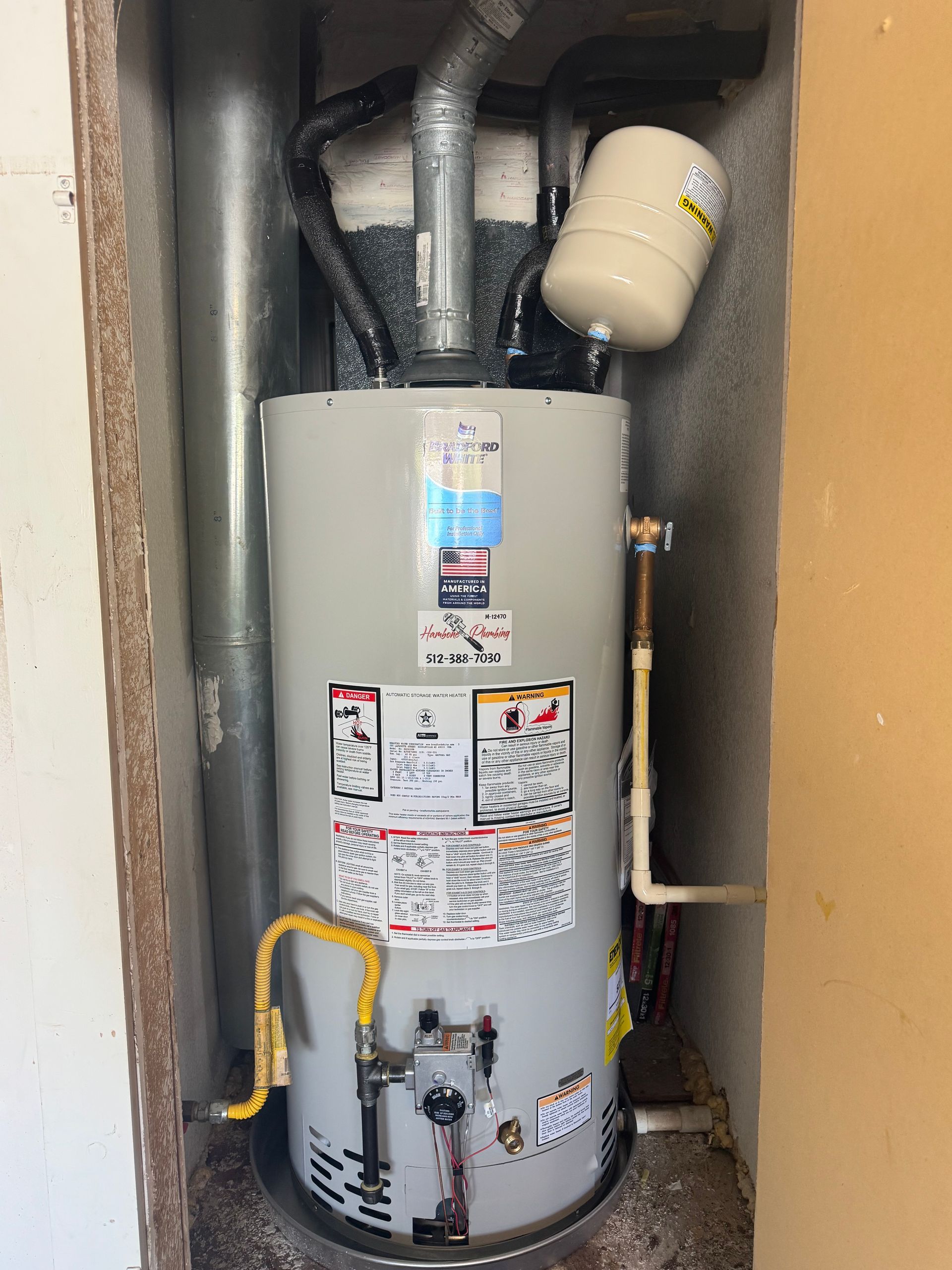 Water heater in a narrow utility closet with pipes, labels, and a yellow gas line.