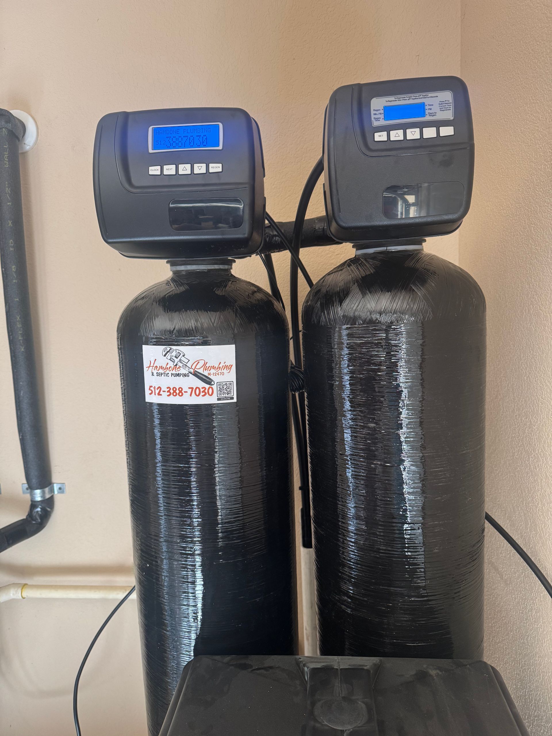 Two black water softener tanks with digital control heads in a utility room