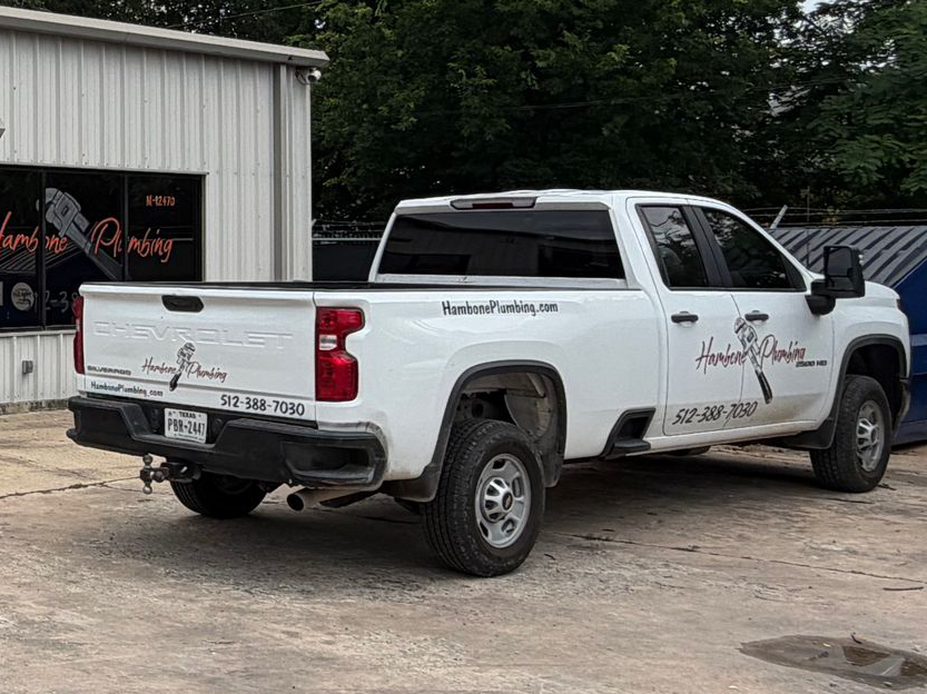 White pickup truck is parked beside a metal building on a gravel lot