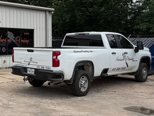 White pickup truck is parked beside a metal building on a gravel lot