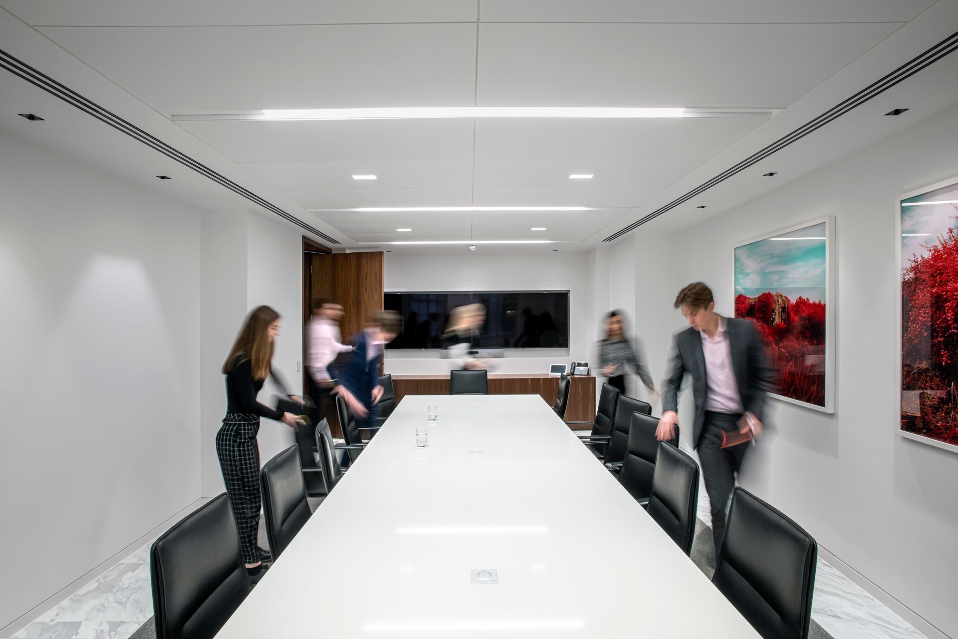Business people entering a bright, modern conference room with a long table and artwork on the walls.
