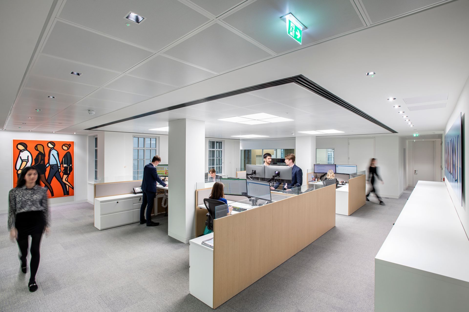 Office interior with workers at desks, modern artwork, and a person walking towards the camera.
