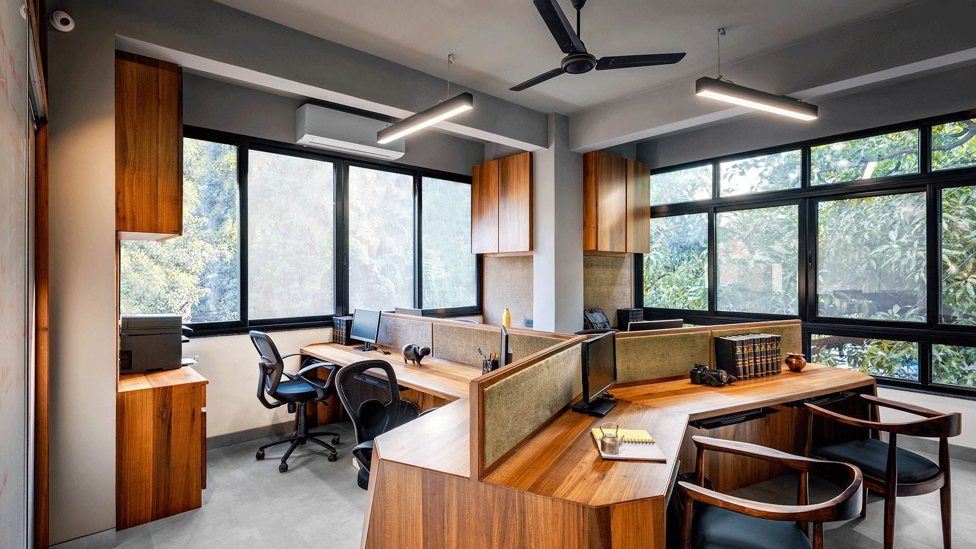 Office interior with wooden desks, chairs, and cabinets. Windows offer a view of trees.