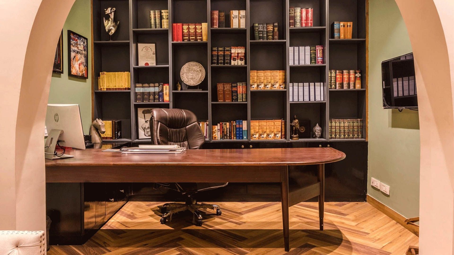 Dark wood desk and bookshelves in a study; green walls, arched doorway, and wooden floors.