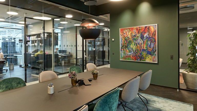 Conference room with long table, chairs, and abstract art on green wall. Glass office spaces are visible.
