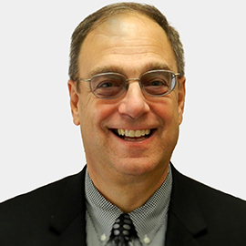 A man wearing glasses and a suit is smiling for the camera